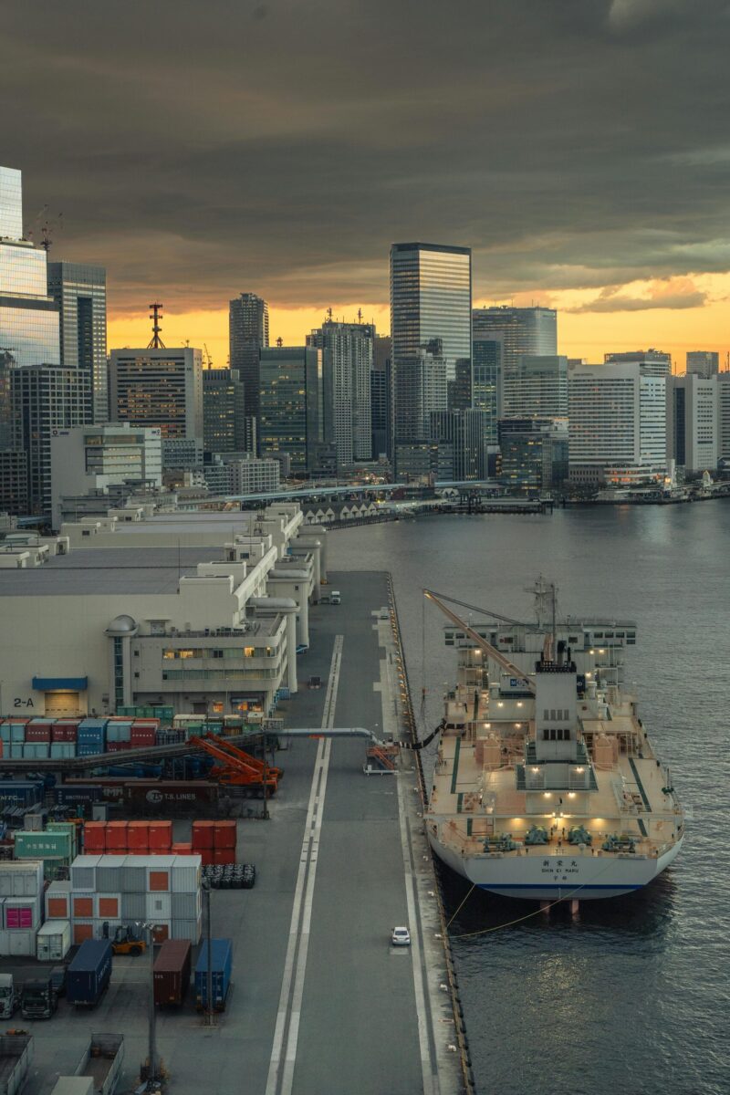 Urban skyline of Tokyo with harbor and ship under a dramatic sunset sky.
